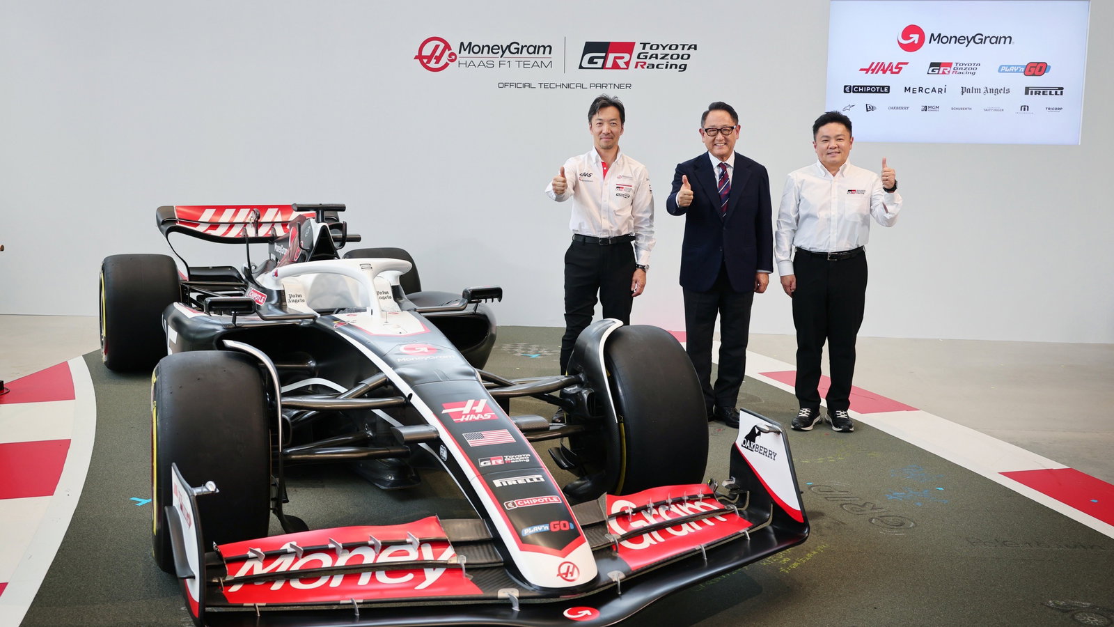 Haas team principal Ayao Komatsu, Toyota chairman Akio Toyoda, TGR president Timoya Takahashi, and a Haas F1 car