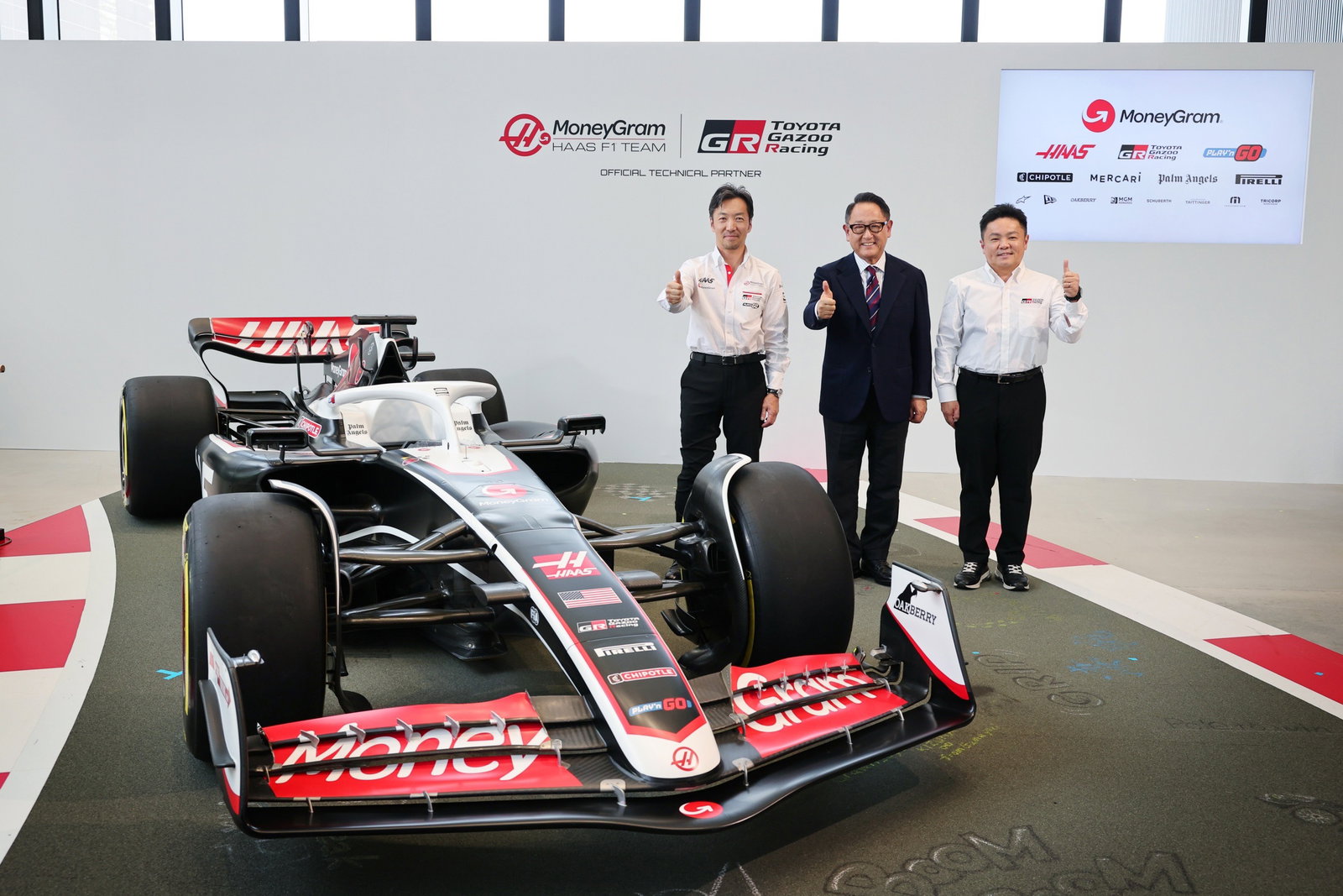 Haas team principal Ayao Komatsu, Toyota chairman Akio Toyoda, TGR president Timoya Takahashi, and a Haas F1 car